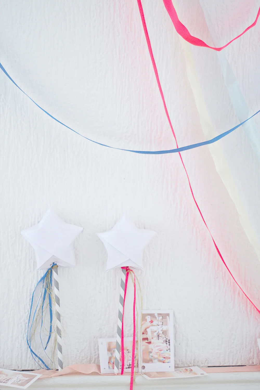 Deux baguettes magiques en forme d'étoiles blanches avec rubans colorés sur un fond blanc décoré de voilages.