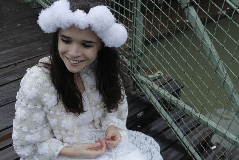 Jeune femme souriante portant une robe et un headband blancs vaporeux, posant sur un ponton en bois.