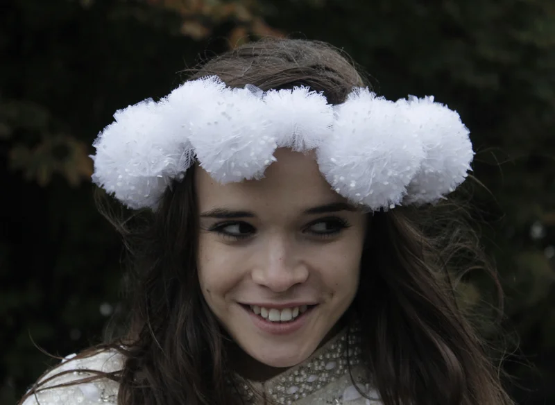 Jeune femme souriante portant un headband floral blanc vaporeux dans ses cheveux bruns.