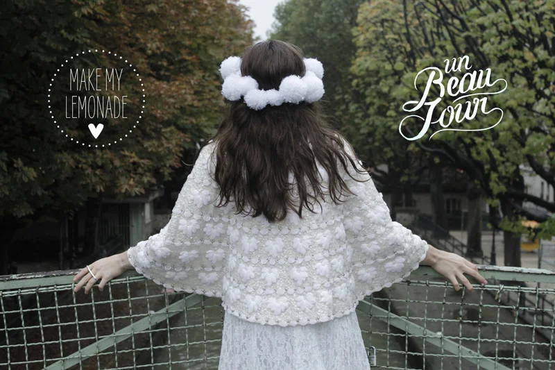 Femme de dos portant un headband de fleurs blanches et un haut texturé blanc, dans un cadre naturel et romantique.