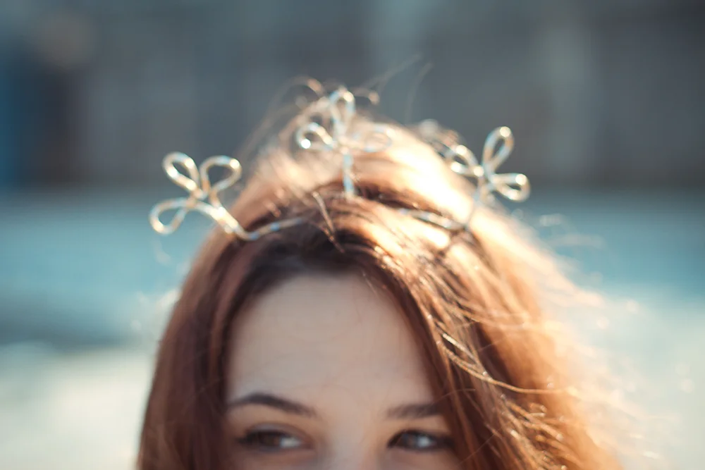 Gros plan flou d'une femme portant une couronne artisanale en fil métallique argenté dans ses cheveux châtains.