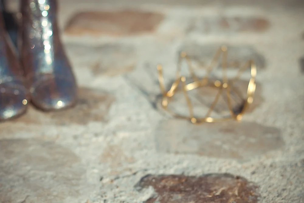 Une couronne dorée minimaliste et des chaussures argentées posées sur un sol en pierre rustique.