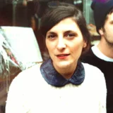 Portrait d'une femme aux cheveux bruns portant un haut blanc avec un col bleu foncé.