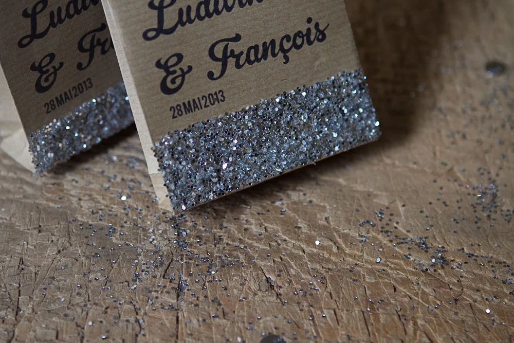 Sachets en papier kraft personnalisés et décorés de paillettes argentées sur un fond en bois rustique.