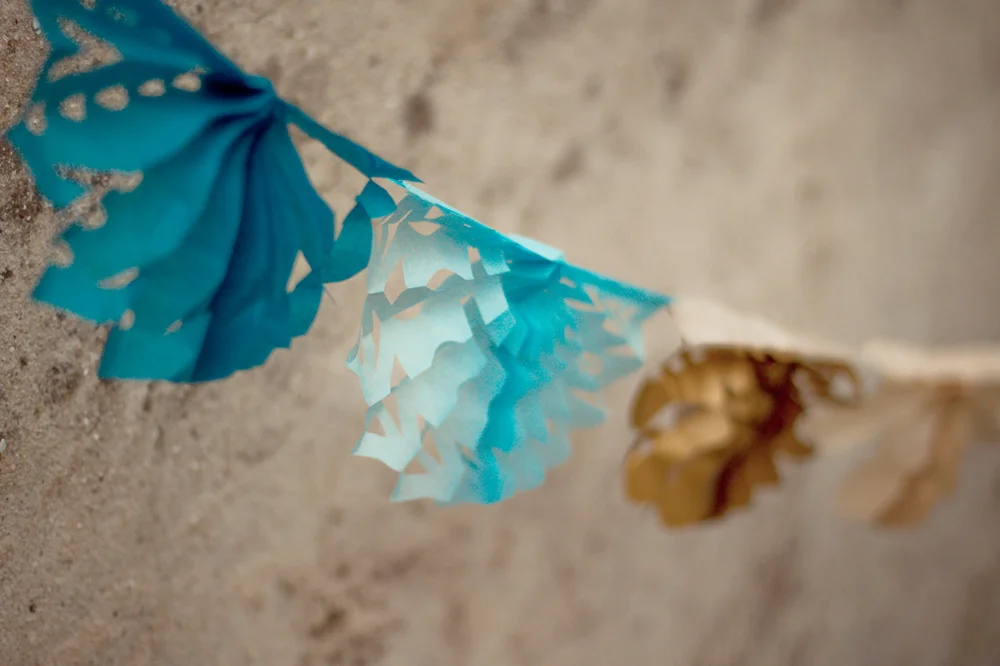 Guirlande de dentelles de papier découpées en formes de feuilles dans des tons de bleu et doré sur fond neutre.