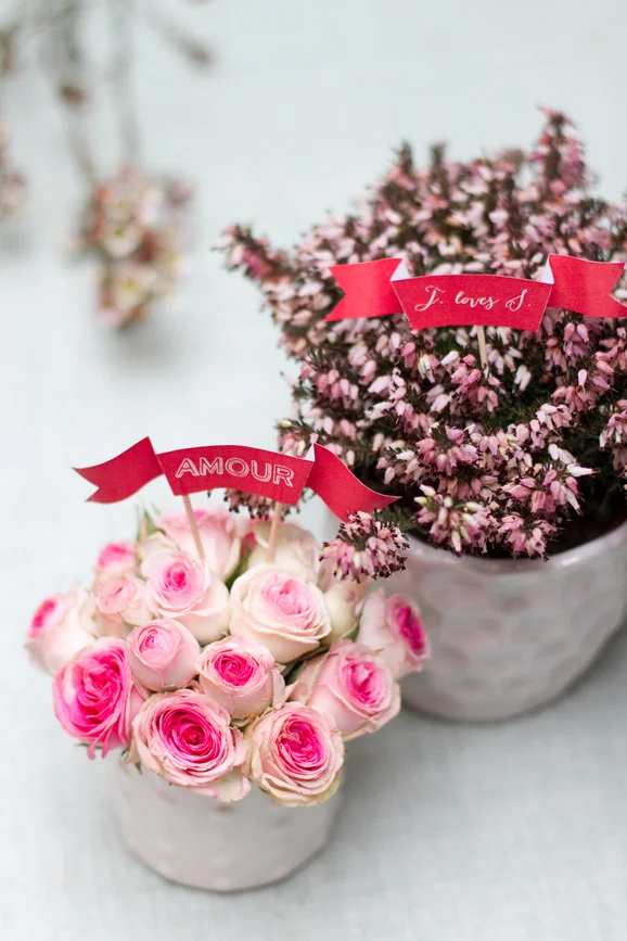 Deux petits bouquets de fleurs roses et mauves décorés de banderoles rouges avec des inscriptions romantiques.