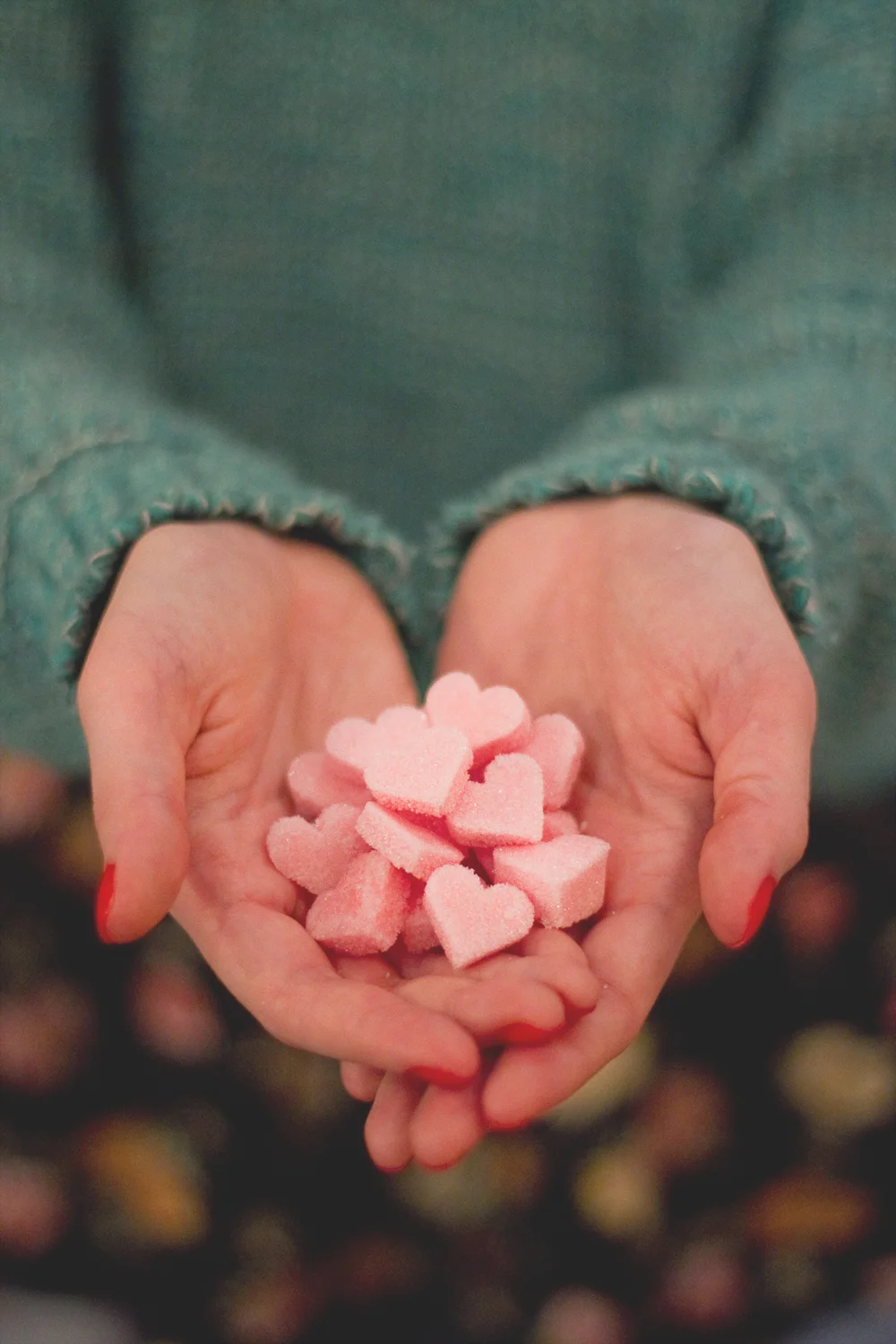 Mains tenant des bonbons roses en forme de cœur, ambiance douce et romantique.