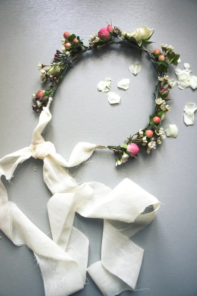 Couronne de fleurs délicates et baies roses avec un long ruban de soie blanc sur fond gris clair.