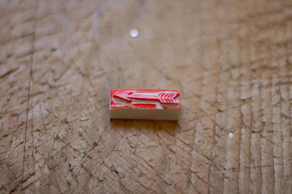 Tampon en caoutchouc rouge et blanc représentant une flèche, posé sur un plan de travail en bois texturé.