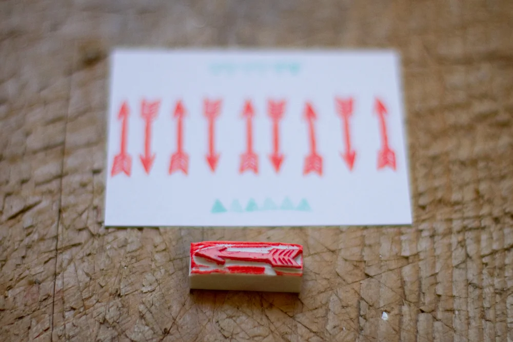 Tampon en caoutchouc rouge et impressions de flèches sur papier blanc posés sur un établi en bois.