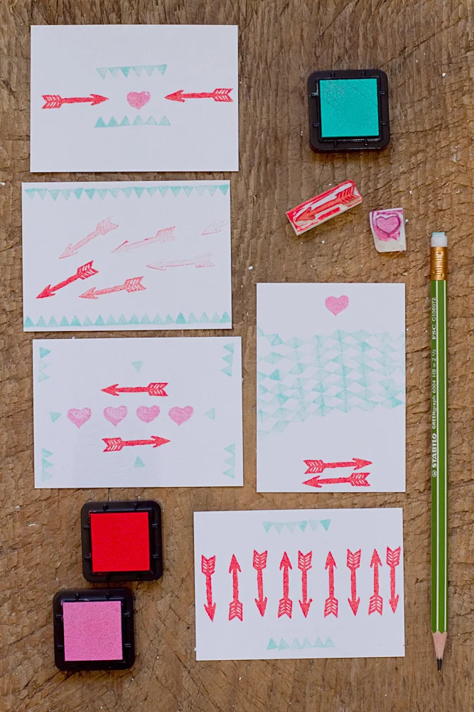 Matériel de stamping avec tampons, encres rouge et turquoise et cartes décorées de cœurs et de flèches sur bois.