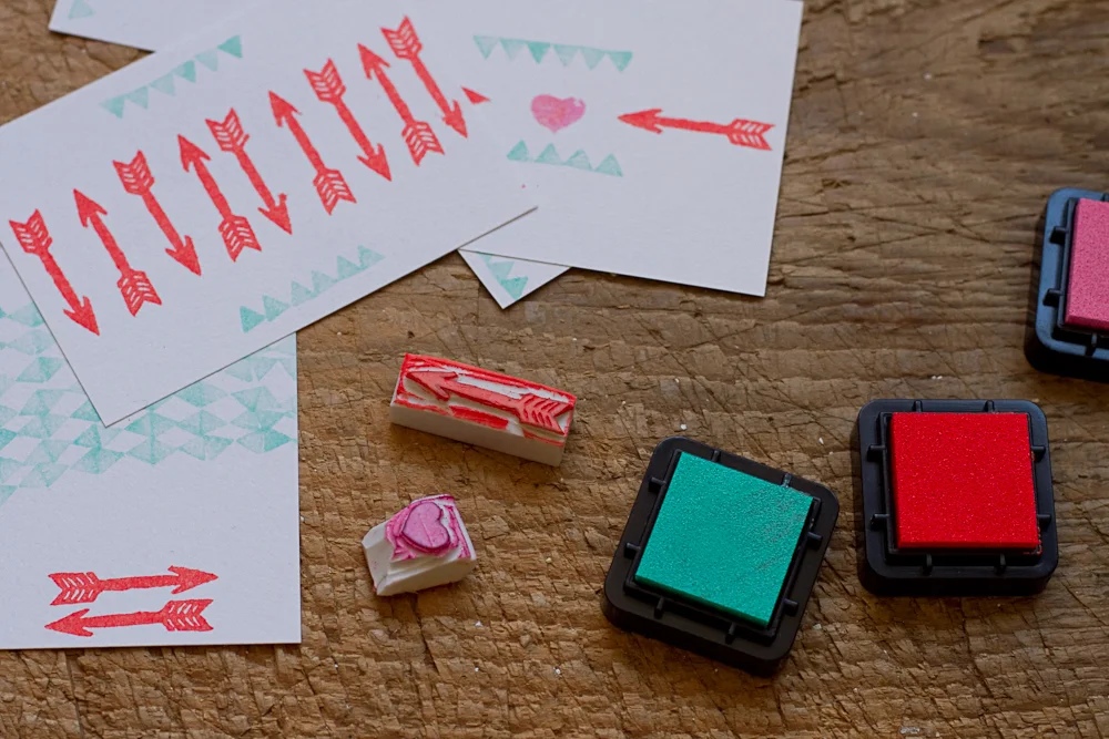 Tampons encreurs rouges et verts et motifs de flèches et cœurs sur papier blanc pour un atelier stamping DIY.