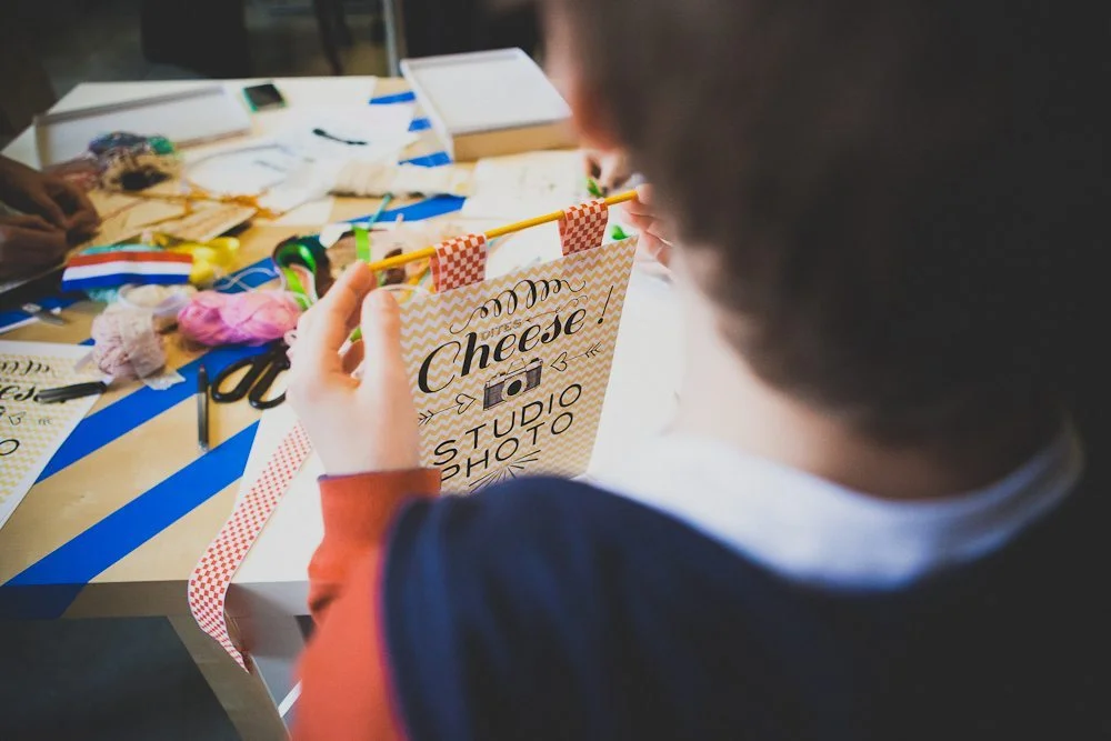 Enfant confectionnant une bannière DIY colorée avec l'inscription Cheese ! Studio Photo sur une table blanche.