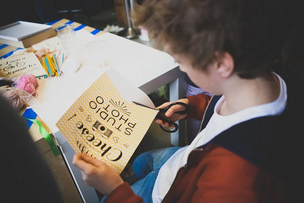 Un enfant découpe une affiche jaune et blanche pour créer une bannière DIY dans une ambiance créative.