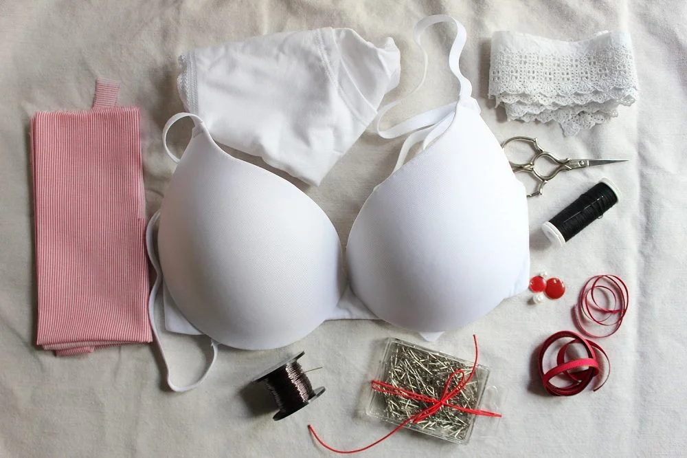 Matériel de couture blanc et rouge, comprenant un soutien-gorge et des accessoires, disposés sur un tissu clair.