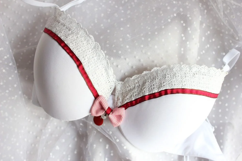 Soutien-gorge blanc avec dentelle et ruban rouge, posé sur un voile léger à pois.
