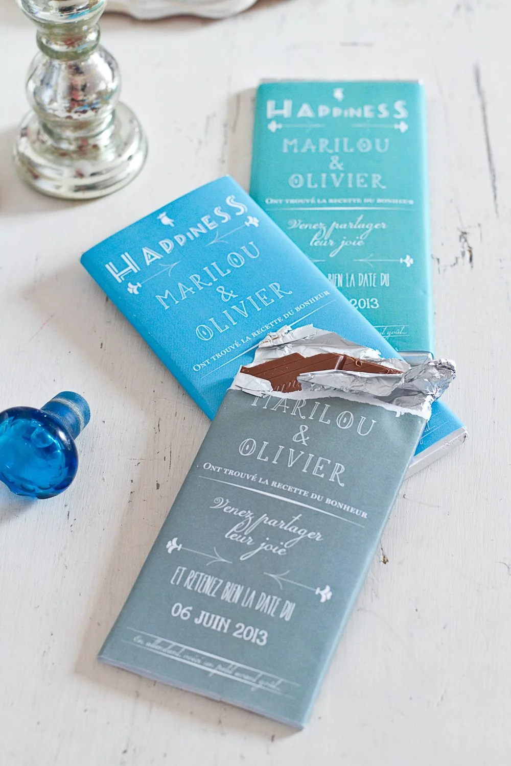 Tablettes de chocolat bleu ciel personnalisées pour un Save the Date, dont l'une est entrouverte sur un fond blanc.