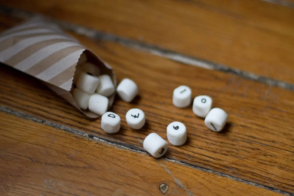 Guimauves blanches marquées de chiffres noirs s'échappant d'un cornet en papier kraft sur une table en bois.