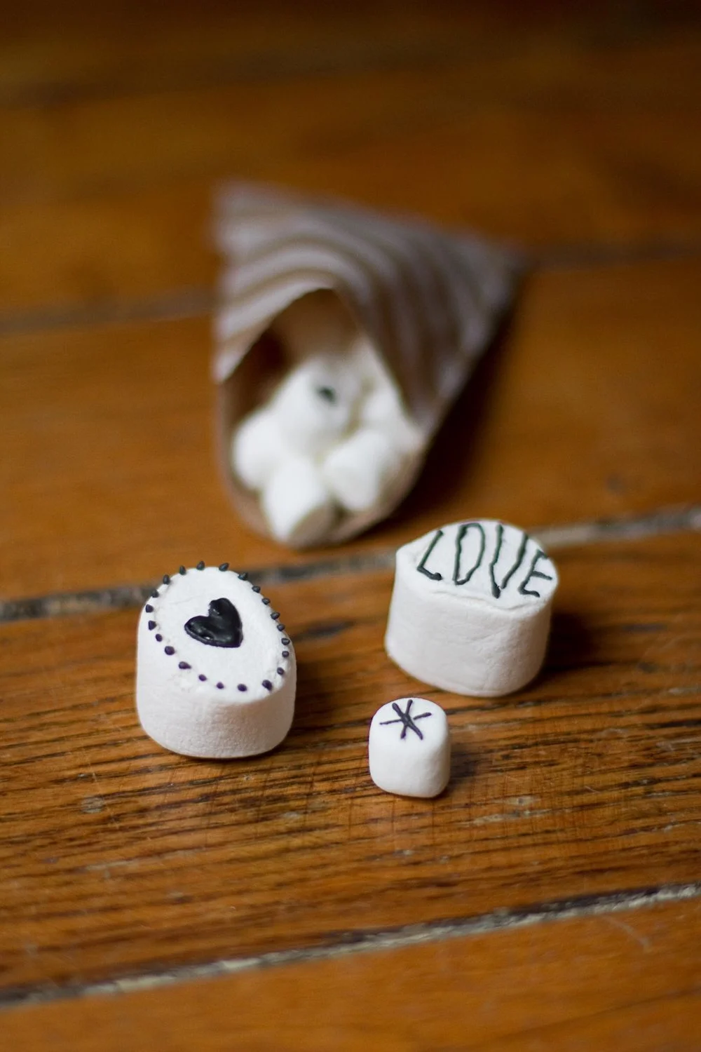 Guimauves blanches décorées d'un cœur et du mot LOVE à l'encre noire sur une table en bois rustique.