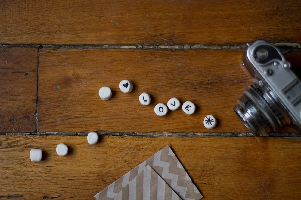Petits bonbons blancs formant le mot LOVE à côté d'un appareil photo argentique sur une table en bois rustique.