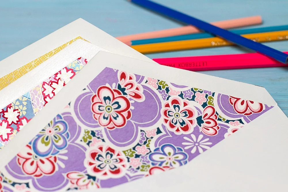Enveloppes de luxe aux motifs floraux colorés et crayons sur un fond bleu clair.