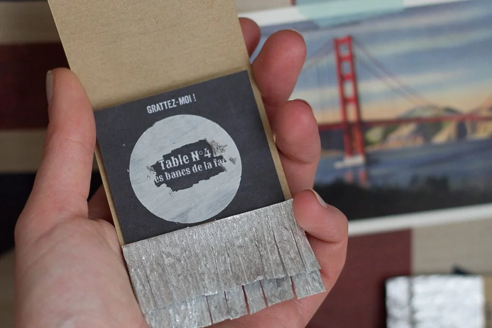 Main tenant un ticket de loterie DIY avec une zone à gratter révélant le numéro de table pour un mariage.