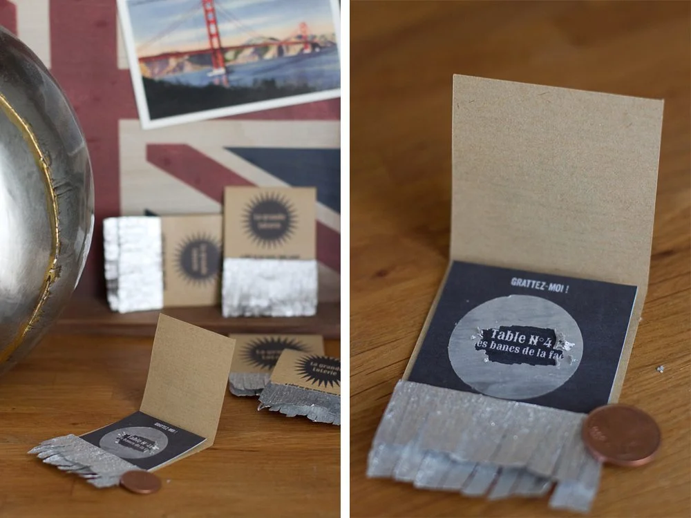 Tickets de loterie faits main en papier kraft et argenté, disposés sur une table en bois.