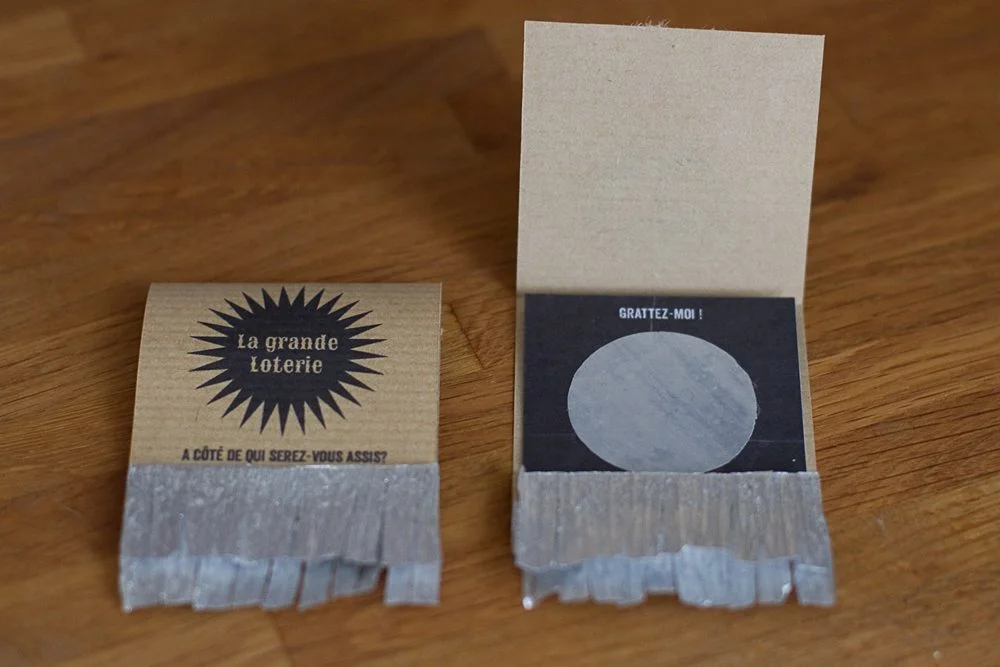 Deux tickets de loterie DIY en carton kraft avec zones à gratter argentées, posés sur une table en bois.