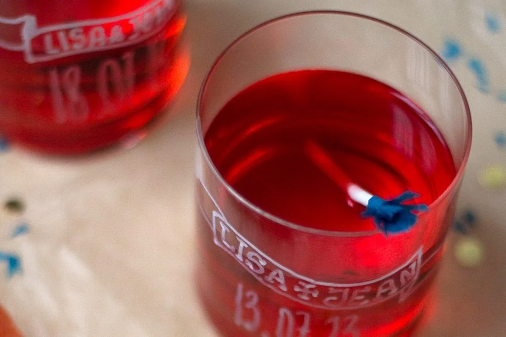 Gros plan de verres remplis d'un cocktail rouge, personnalisés à l'écriture blanche avec les prénoms Lisa et Jean.