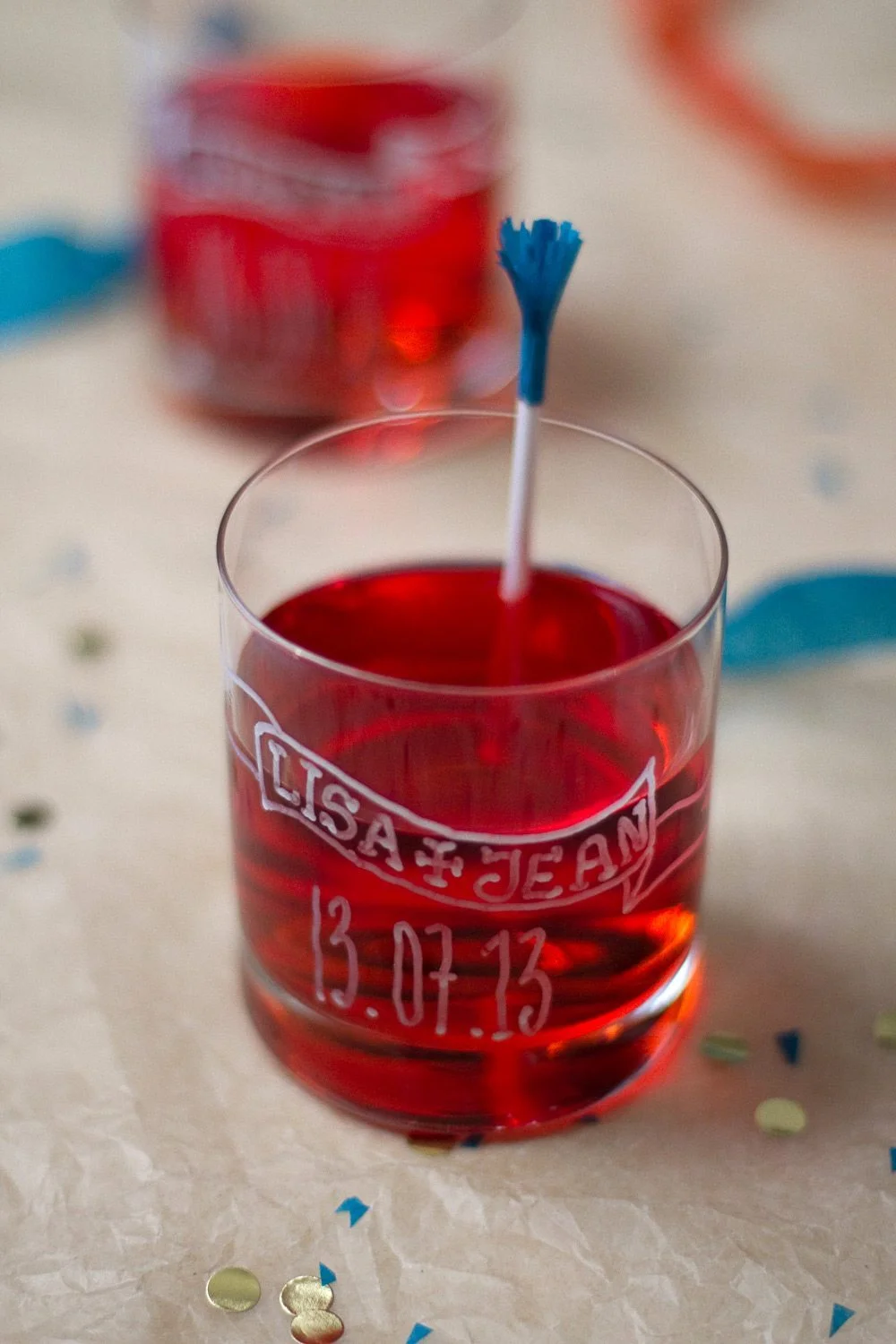 Verre personnalisé avec les prénoms Lisa et Jean et une date, rempli d'un liquide rouge avec un mélangeur bleu.