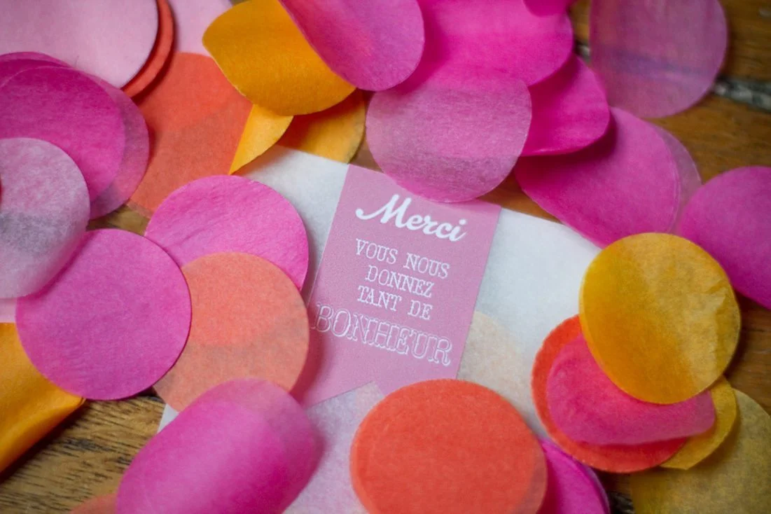 Confettis colorés en papier de soie entourant une petite carte rose avec l'inscription Merci.