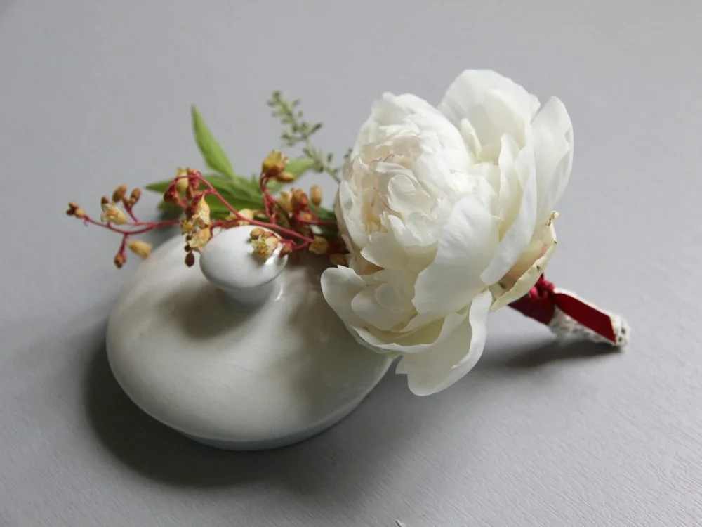 Boutonnière composée d'une pivoine blanche et de petites fleurs jaunes sur un couvercle en céramique blanche.