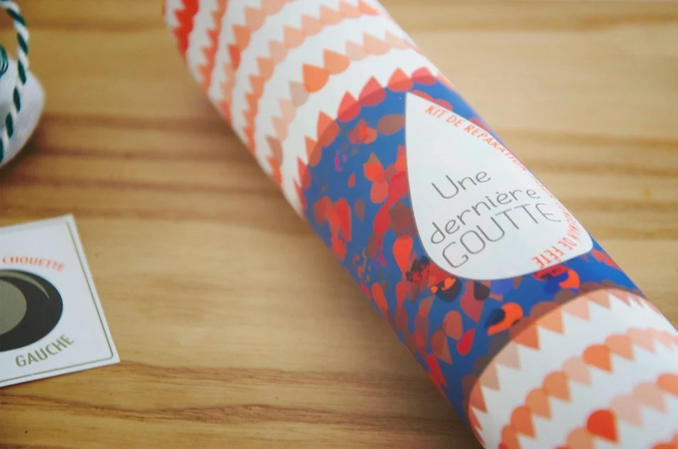 Tube en carton décoré de motifs colorés et d'une étiquette « Une dernière goutte » posé sur une table en bois.
