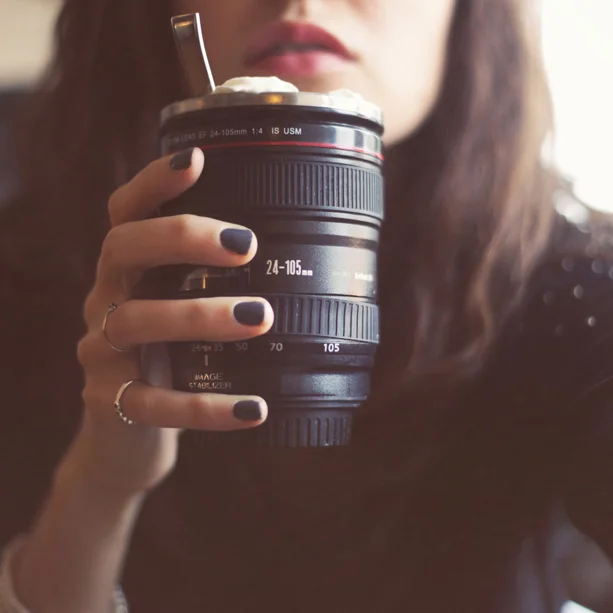 Une femme tient un dessert glacé servi dans un objectif d'appareil photo détourné en verre.