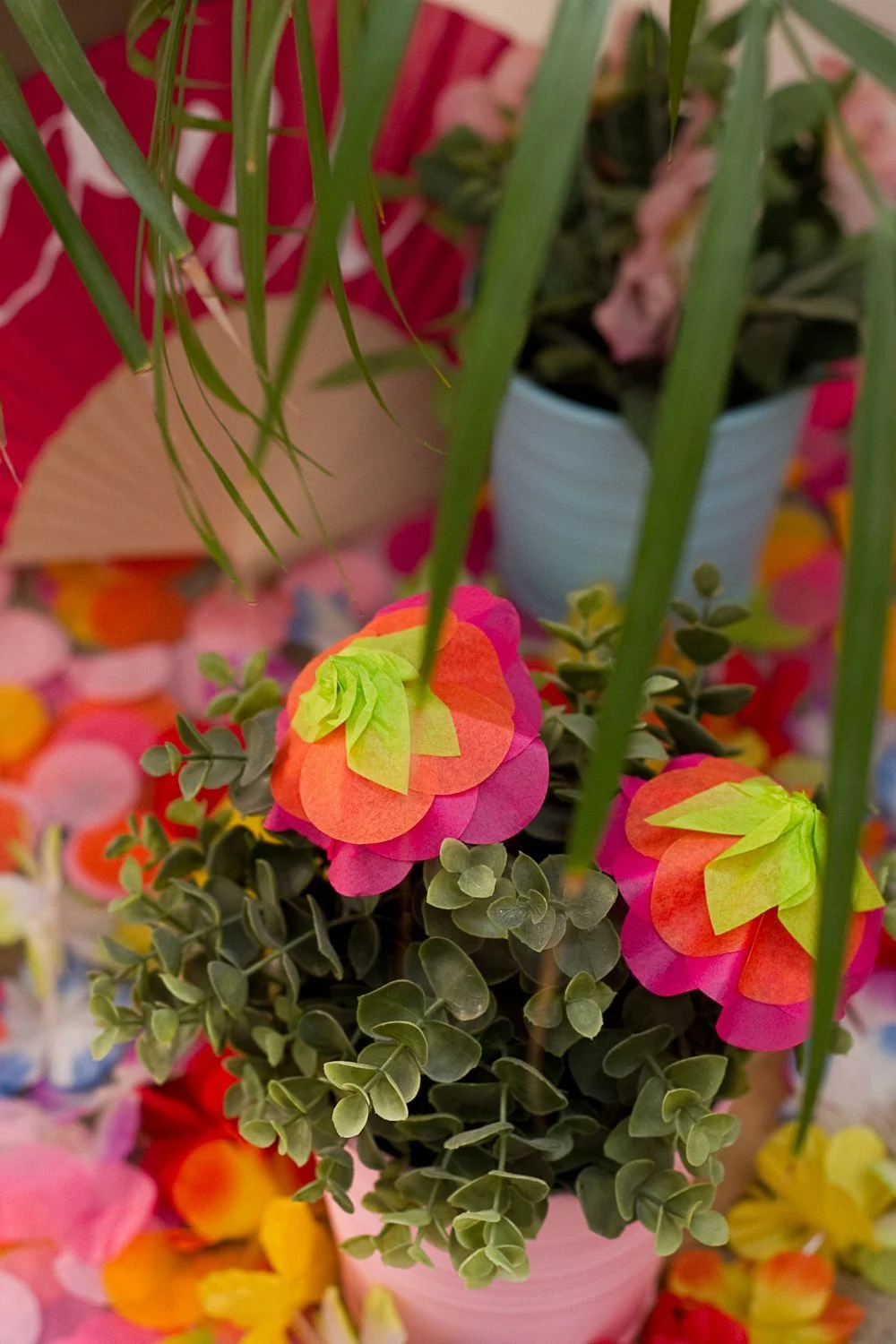 Composition festive de fleurs en papier colorées et feuillage vert dans un pot rose, ambiance DIY et printanière.