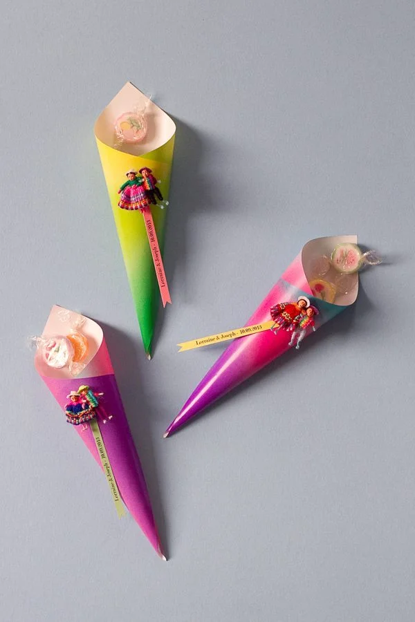 Trois cornets colorés en dégradé contenant des dragées et décorés de figurines péruviennes et de rubans personnalisés.