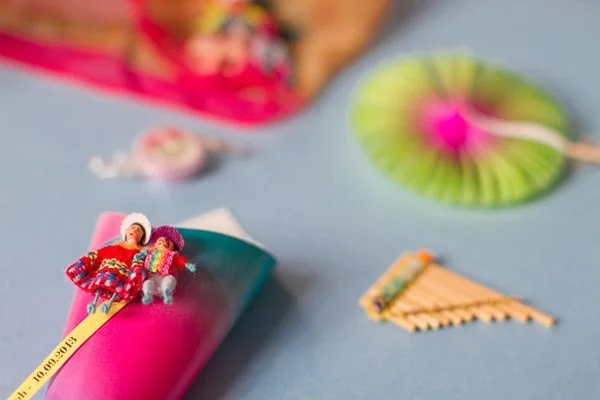 Petites figurines péruviennes colorées posées sur un cornet rose et bleu, entourées d'accessoires festifs.