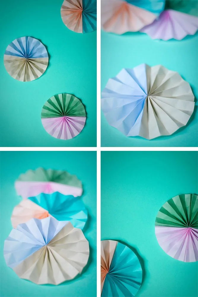 Rosaces en papier plissé pastel et colorées disposées sur un fond turquoise vif.