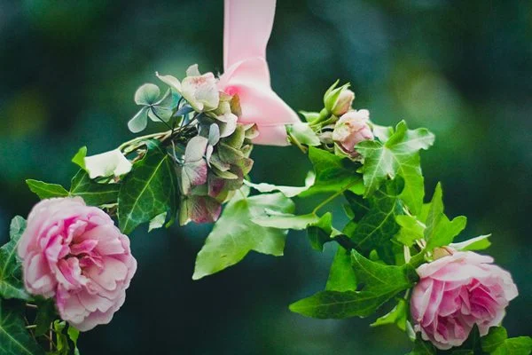 Couronne végétale romantique composée de roses roses, de feuilles vertes et d'un ruban rose satiné.