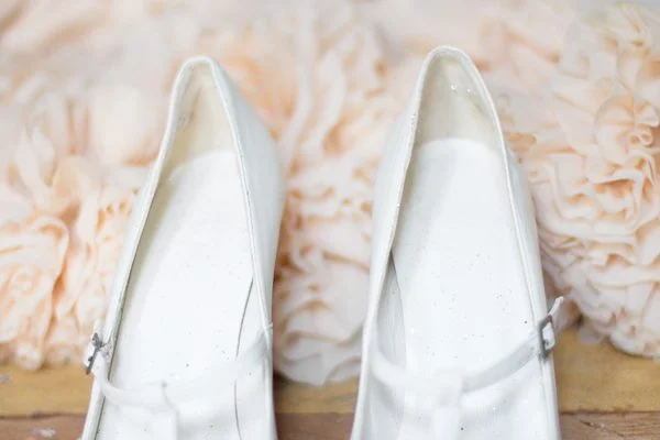 Paire de chaussures blanches élégantes posées devant un fond de fleurs en tissu crème.