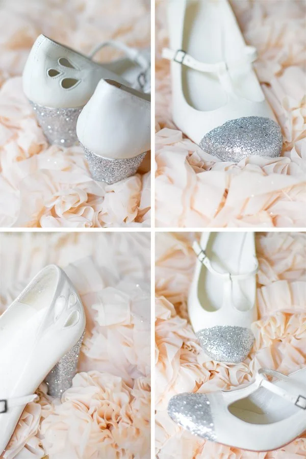 Chaussures blanches à talons avec bouts pailletés argentés, posées sur un tissu vaporeux couleur pêche.