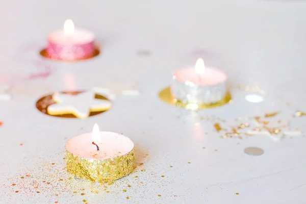 Trois bougies chauffe-plat allumées et des paillettes dorées sur un fond blanc pour une ambiance festive et romantique.