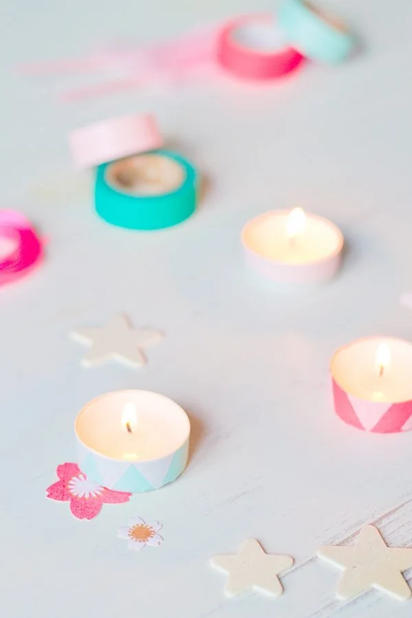 Bougies chauffe-plat colorées en pastel et étoiles décoratives sur un fond blanc lumineux et épuré.