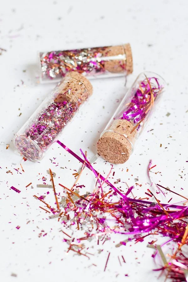 Trois tubes à essai bouchonnés remplis de confettis brillants roses et argentés sur un fond blanc épuré.