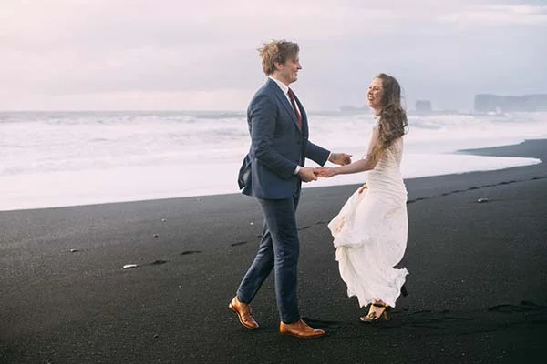 Un couple heureux dans des costumes de mariage romantiques sur une plage de sable noir, inspirant des idées pour un