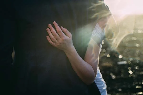 Un couple tendrement s'embrassant au crépuscule, avec la main de la femme portant un anneau de mariage, évoquant la