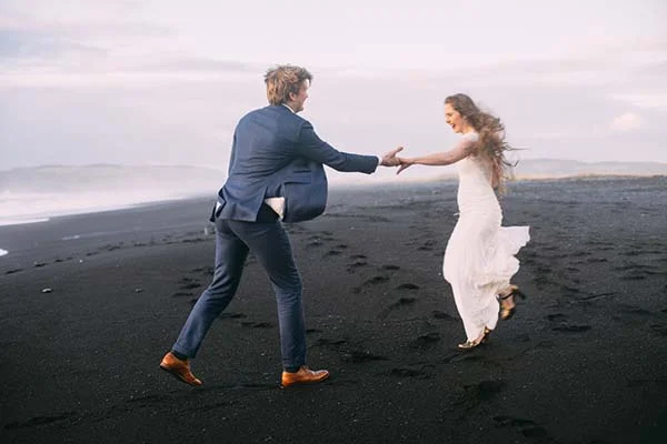 Un couple heureux dans des costumes romantiques contre un décor époustouflant de plage noire et plaine montagneuse.