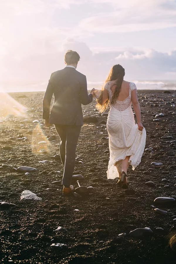 Un couple romantique se promène sur une plage rocheuse, baigné de lumière dorée du coucher du soleil.