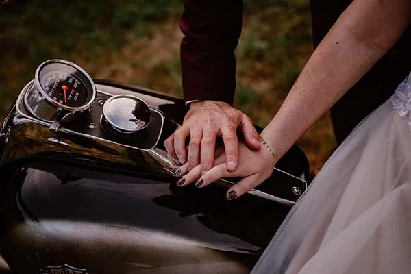 Une main de mariée et de marié, posées sur une moto Harley Davidson, incarnant l'élégance et l'excitation d'un mariage
