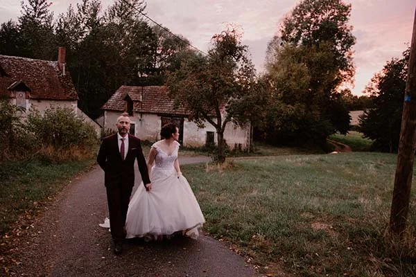 Une mariée et un mari en robe noire et cravate rouge marchent dans un parc romantique au crépuscule, inspirant des